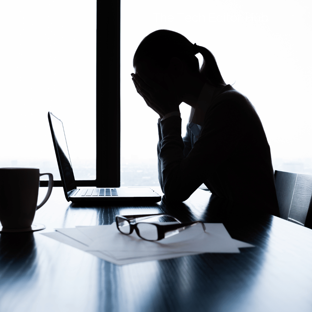 Silhouette of a woman sitting at a desk in front of a computer with her head in her hands