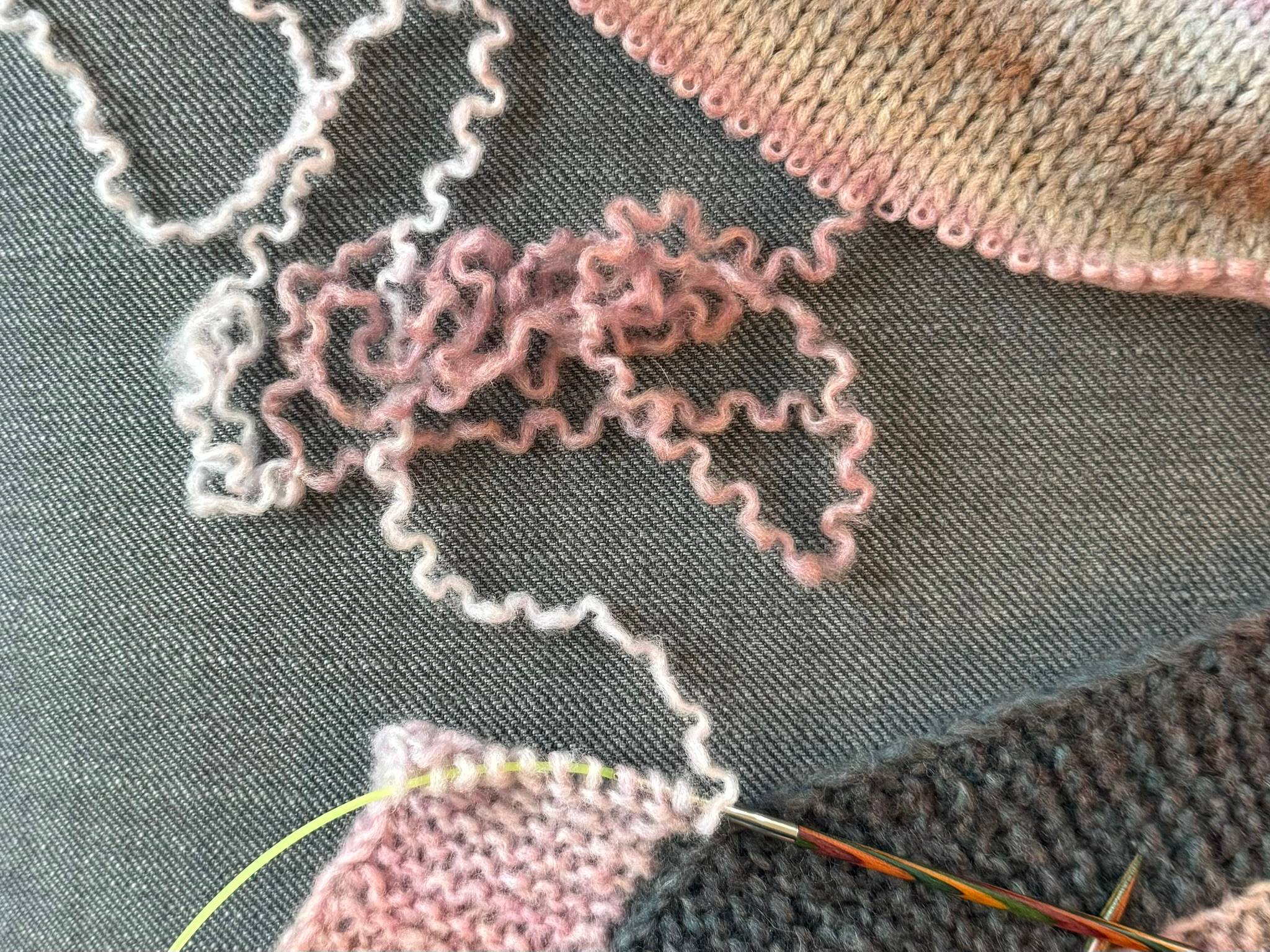 A piece of knitting is half frogged and being knit into something else