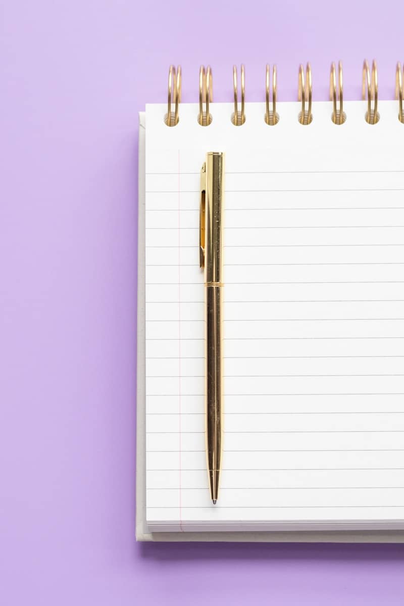 White spiral notebook and gold pen on purple background.