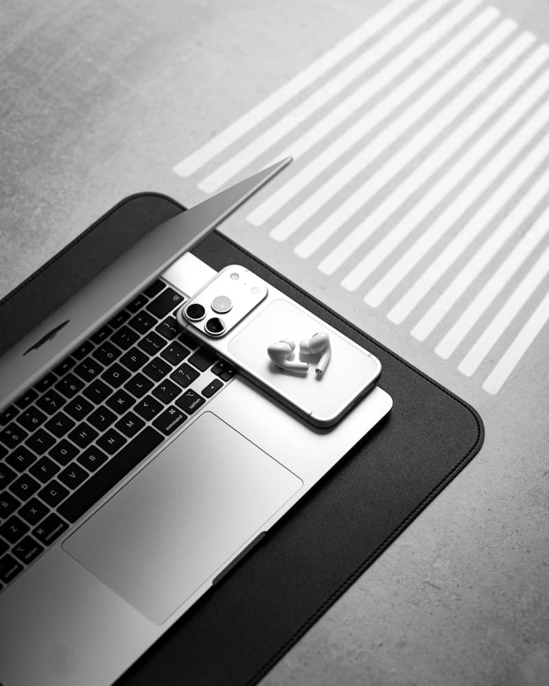 Laptop, smartphone, and earbuds on a desk with striped light.