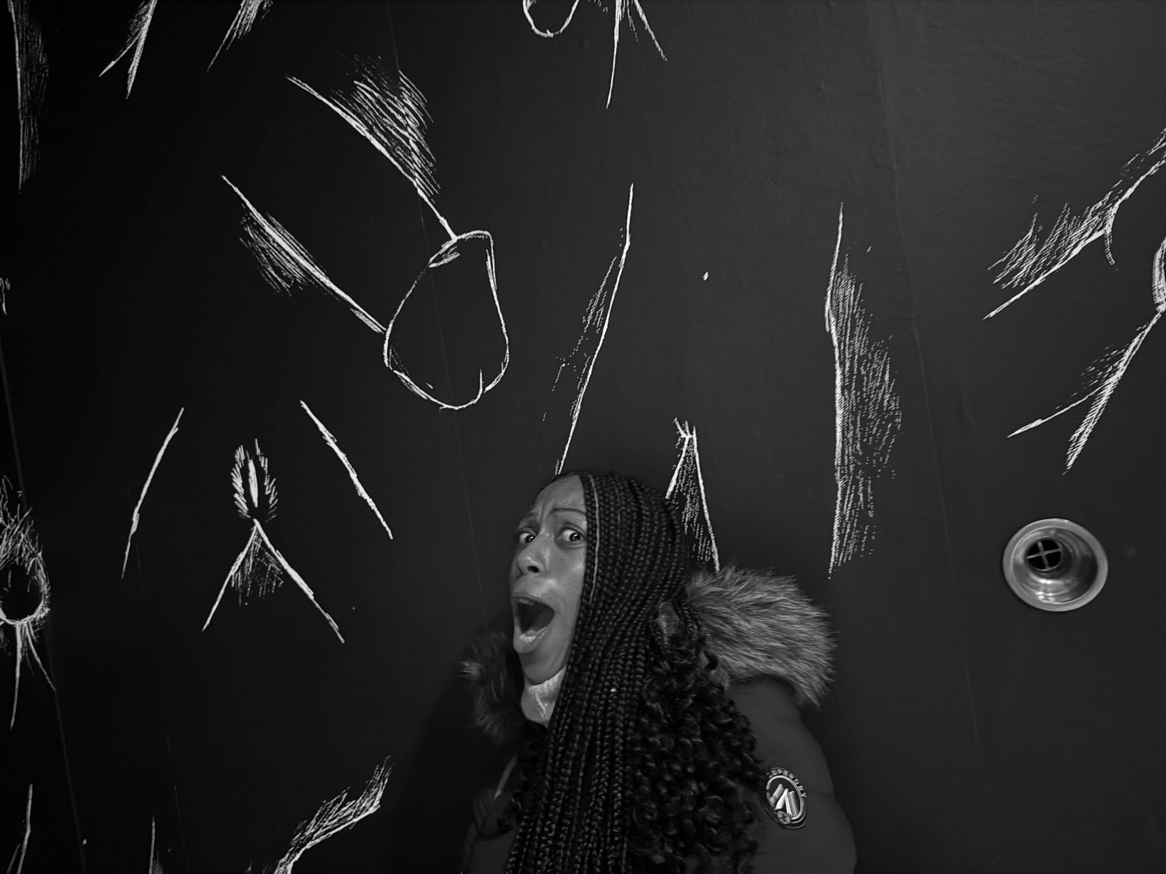 Maria appears shocked while standing in front of an art wall of drawn penises