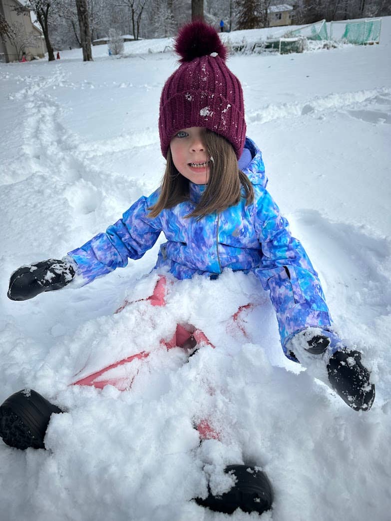 A girl sitting in the snow smiling because she dressed well for winter