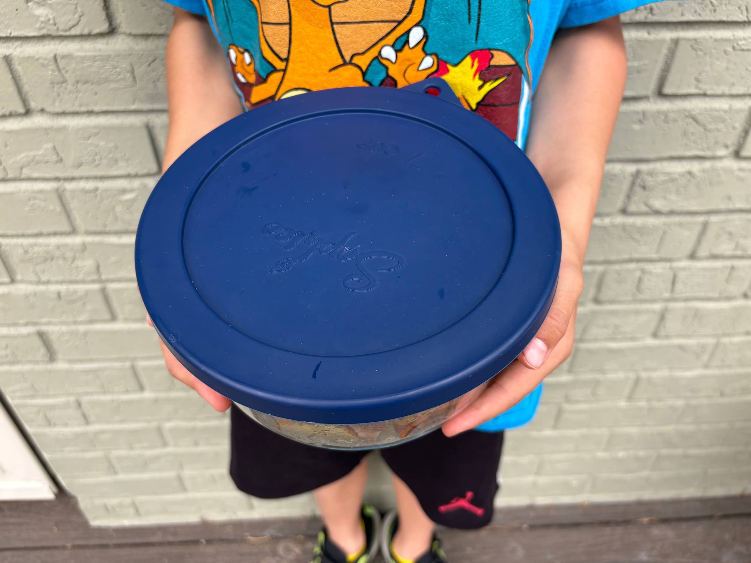 One of my young sons holds a round glass Pyrex dish with a blue lid filled with a homemade meal, moments before we walked it across the street to our elderly neighbor.