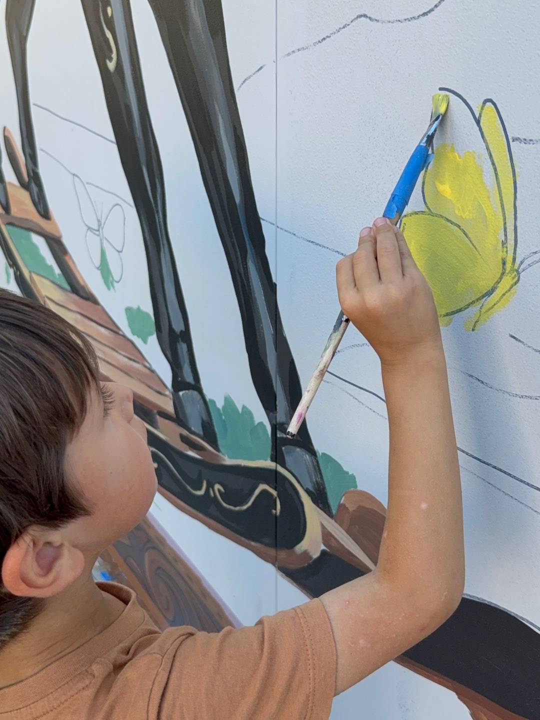 A child helps paint the new Colorado Baby mural, adding bright yellow paint to a butterfly on the side of the building.