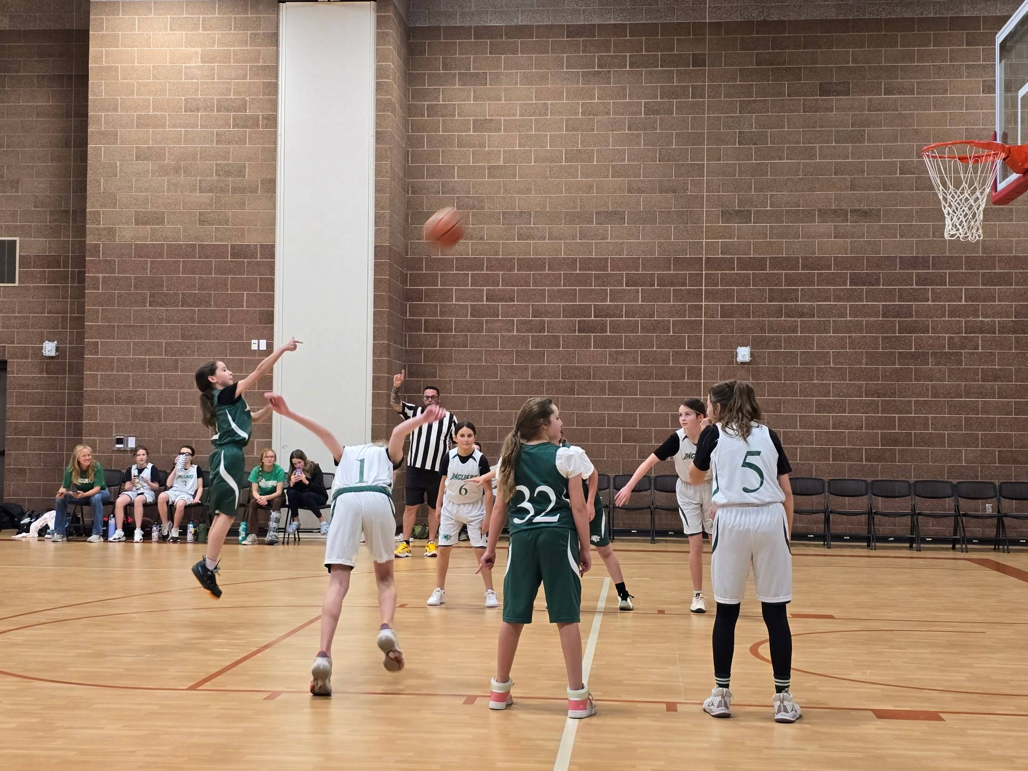 girls playing basketball, at a moment of a free throw shot. The shooter is jumping high while taking her shot.