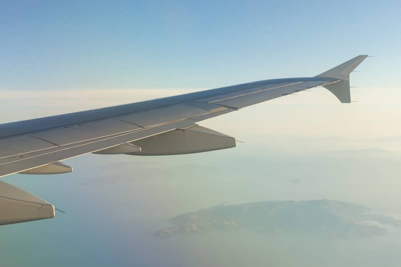 Airplane wing soaring over ocean and distant land.