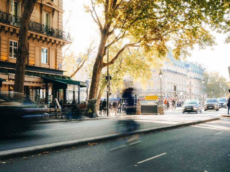 Busy city street with blurred cars, people, and historic buildings.