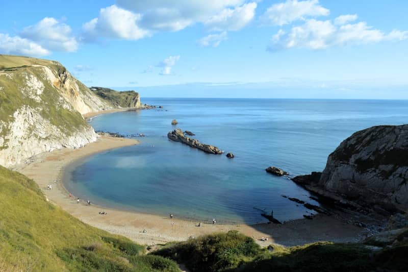Coastal bay with white cliffs, sandy beach, and blue sky.