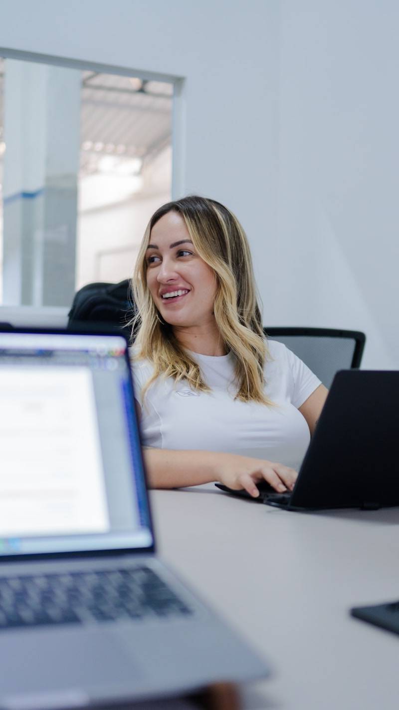 A woman smiles while working on her laptop.