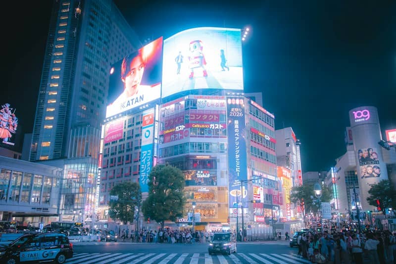 Crowded street intersection at night with illuminated billboards and taxis in Shibuya, Tokyo