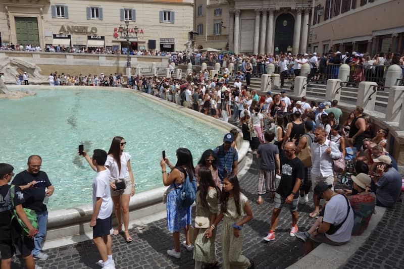 Crowds gather around a fountain on a sunny day.