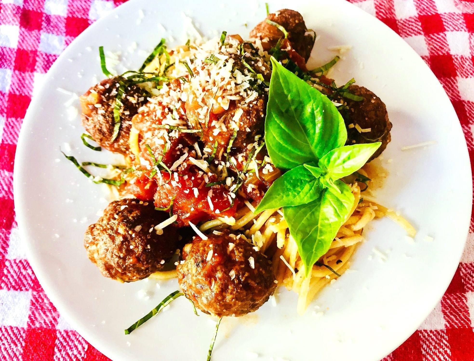 Spaghetti Meatballs on a white plate with fresh basil as garnish 