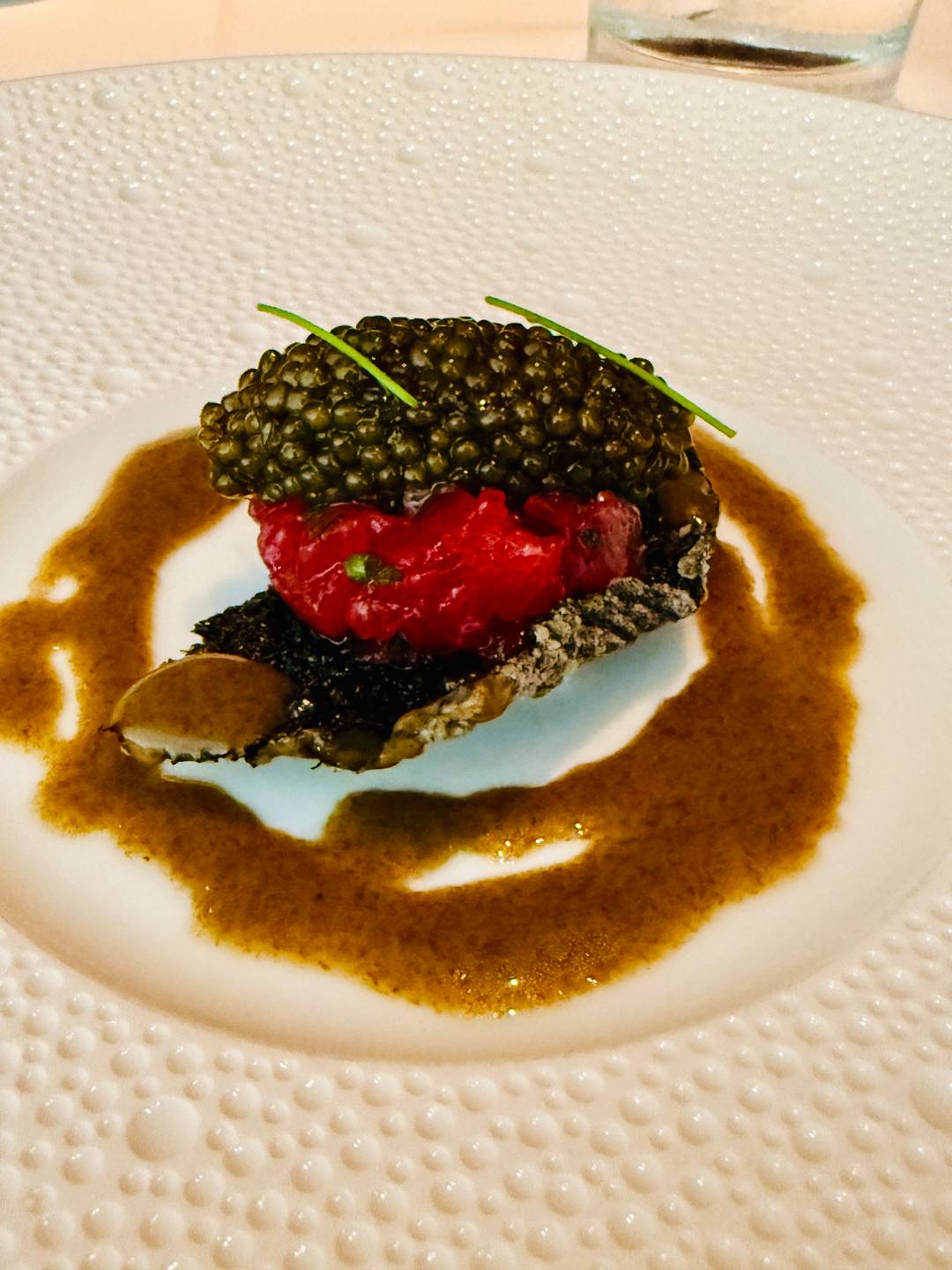 An exquisite caviar and tartare dish at Le Bernardin, plated with a delicate sauce swirl on the left, two pieces of large, crispy fried chicken with mashed potatoes and Kale from Red Rooster on the right
