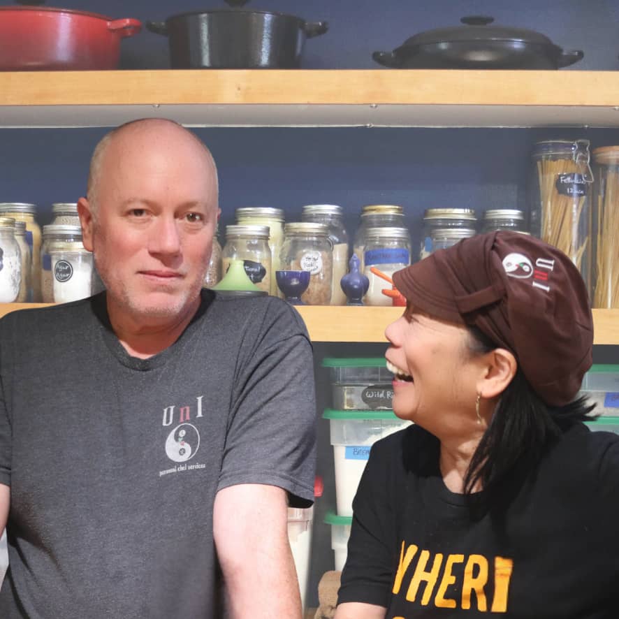 Aric and Yukari in front of pantry shelves, smiling and laughing.