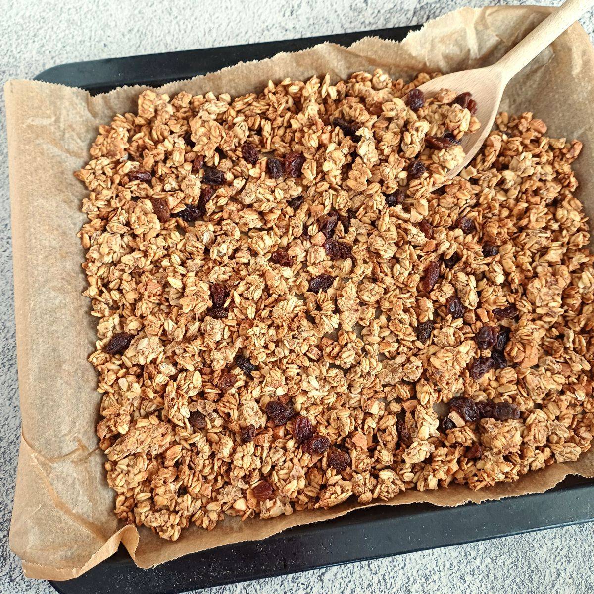 banana granola on a lined baking sheet with a wooden spoon in it.