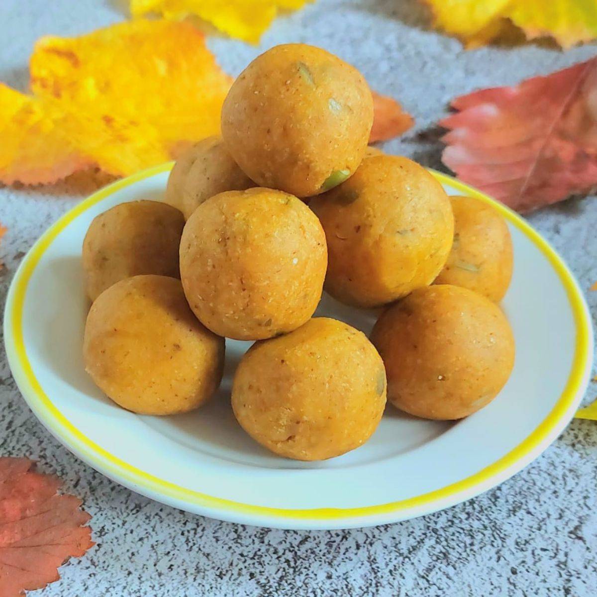 no bake pumpkin energy balls arranged on a white plate placed on a granite with autumn leaves around it.