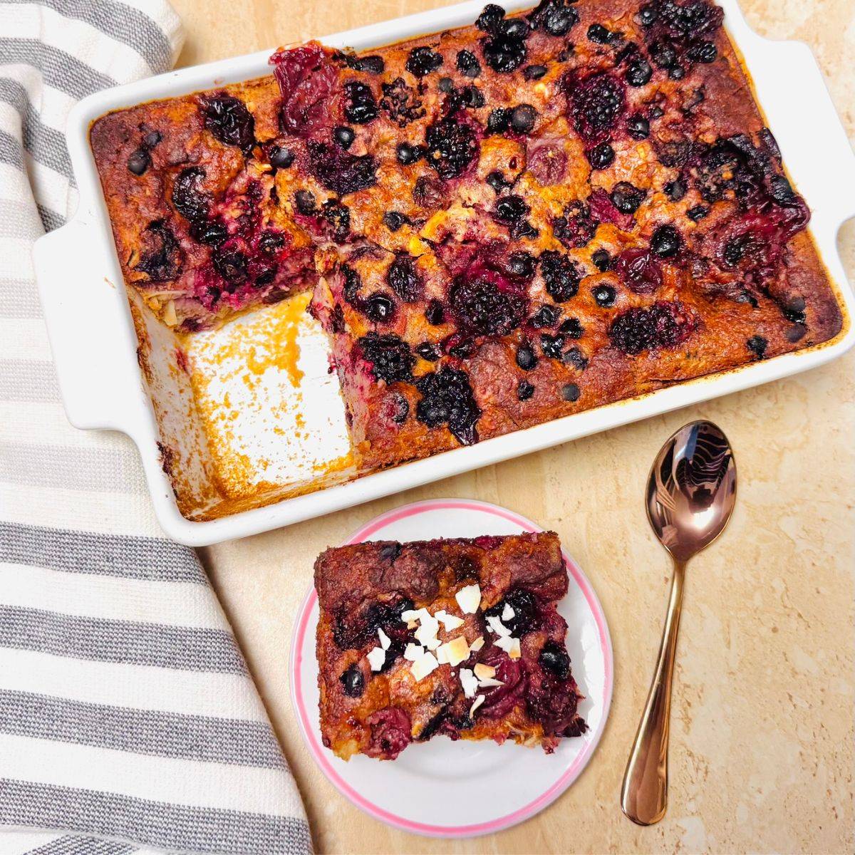 white plate of slice of black forest fruit baked breakfast oatmeal on a brown tile along with a spoon
