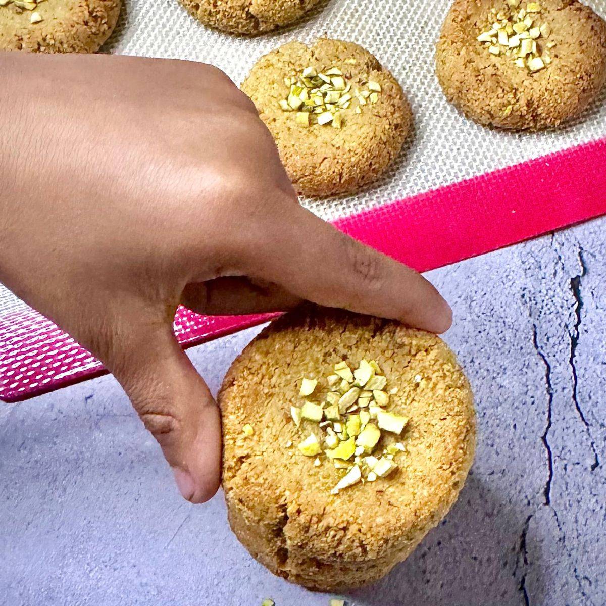 Child holding pistachio almond flour biscuit from the stack.