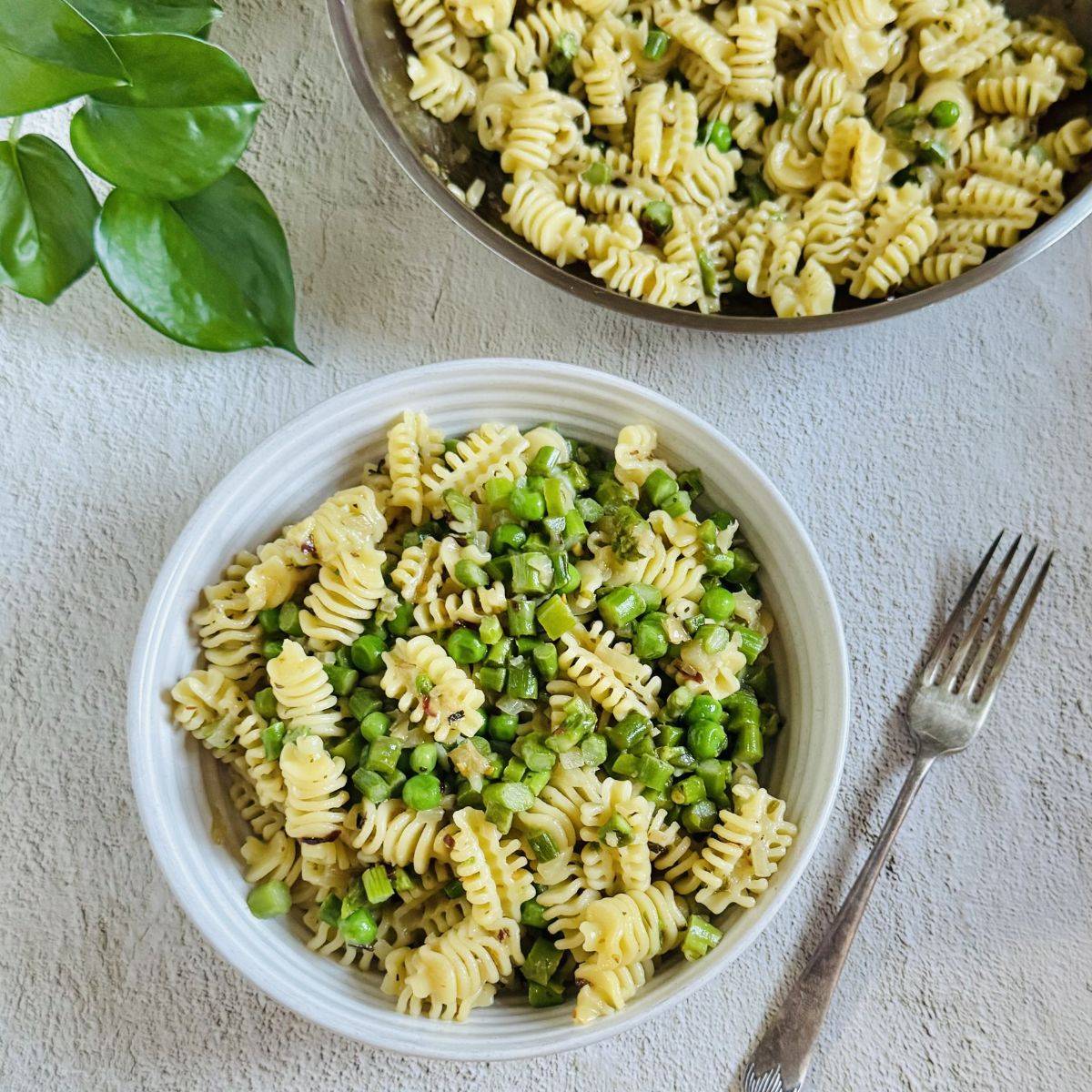 bowl of asparagus pea pasta with a fork and a pan of pasta placed behind it. 