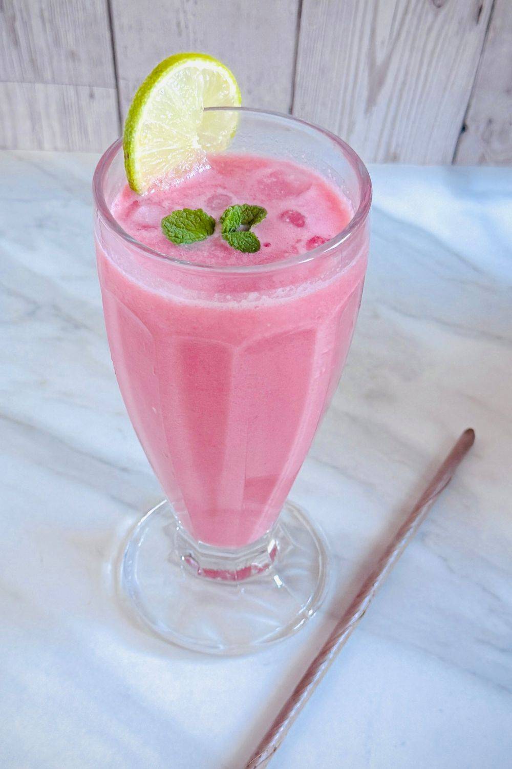 glass filled with watermelon coconut milk cooler placed on marble along with an eco friendly coconut leaf straw.