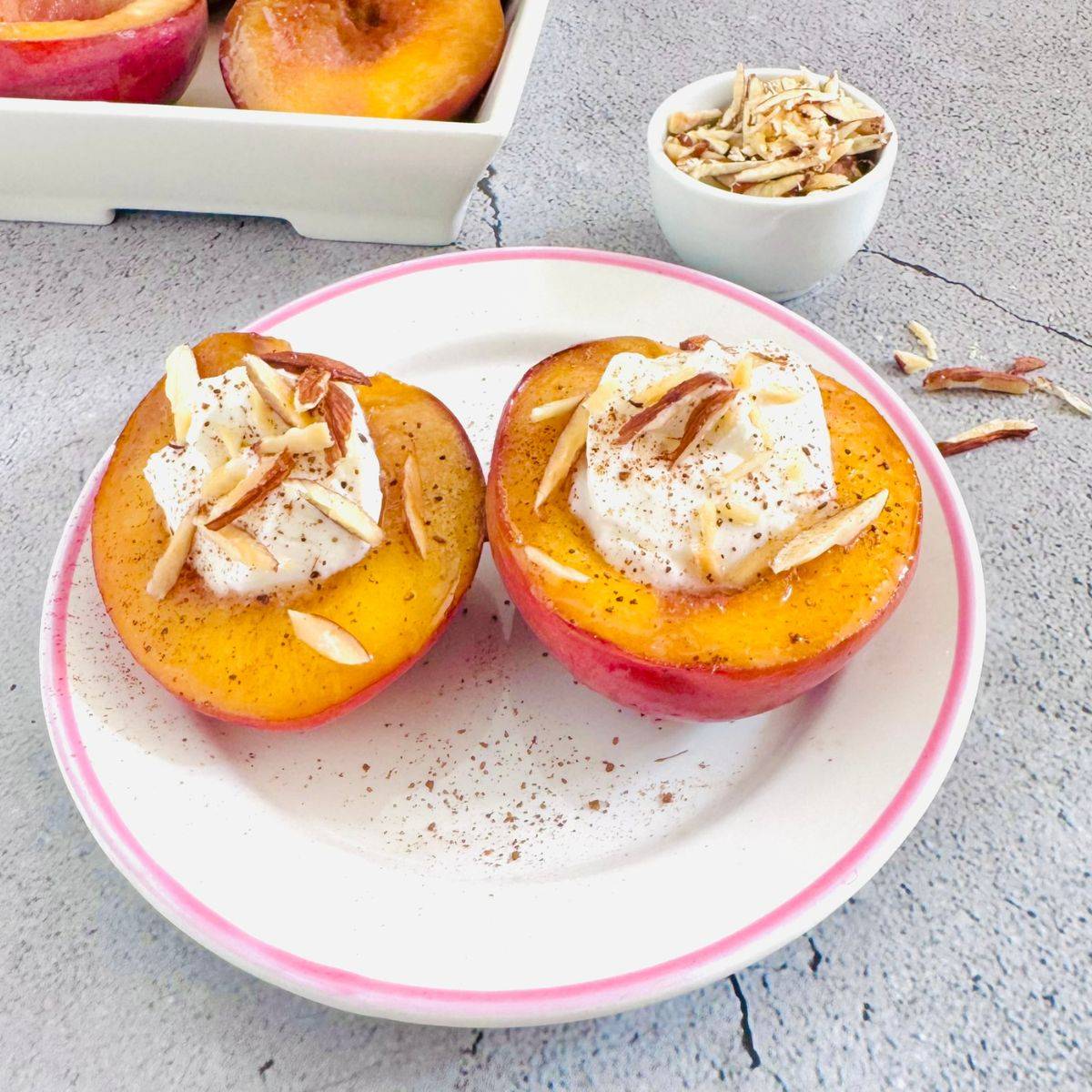 white plate of pan fried two nectarine halves topped with yogurt and almonds.