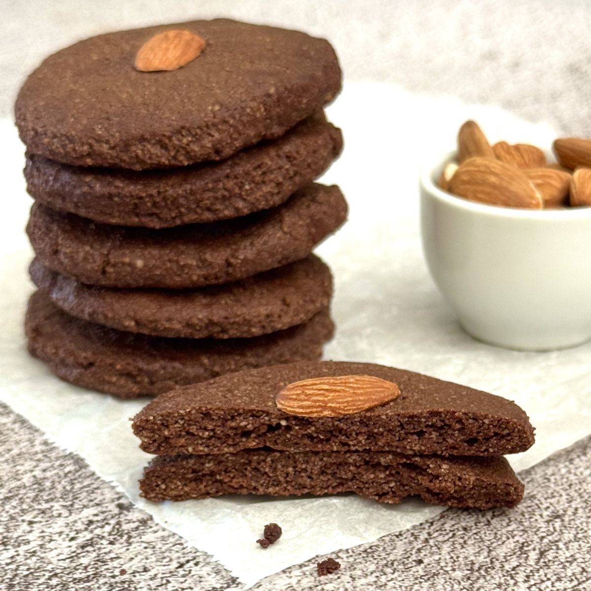 stack of almond flour chocolate cookies with a pinch bowl of almonds behind them.