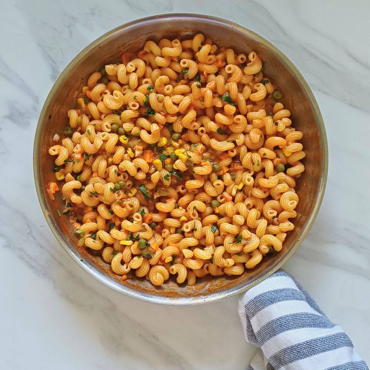 vegetable coconut milk pasta in a wide steel pan placed on a marble with a kitchen towel wrapped around the handle. 