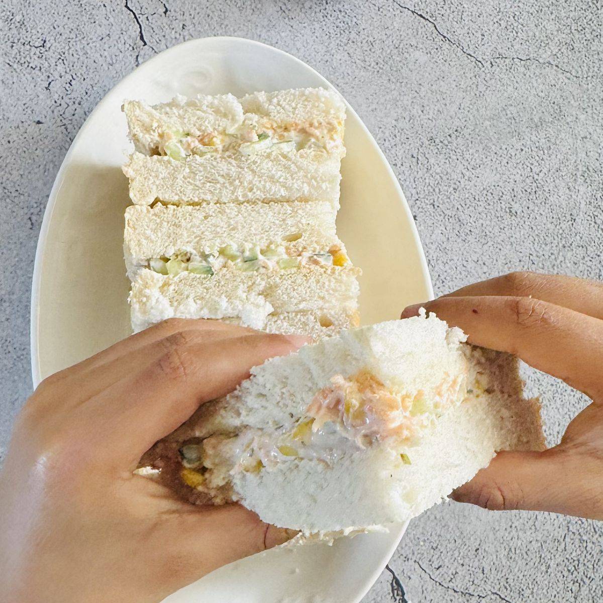 child holding sandwich in his hands on top of a white plate filled with sandwich squares.
