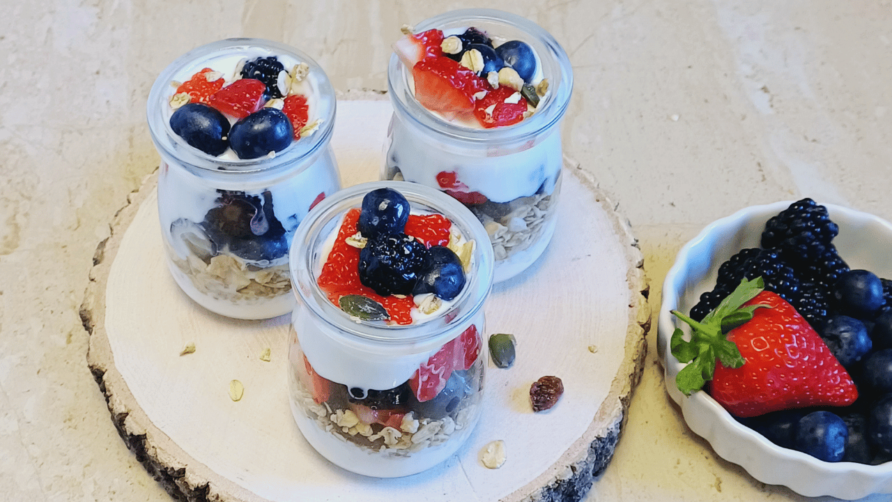 three jars of mixed berry yogurt parfait placed on wooden block along with a small bowl of fresh berries.