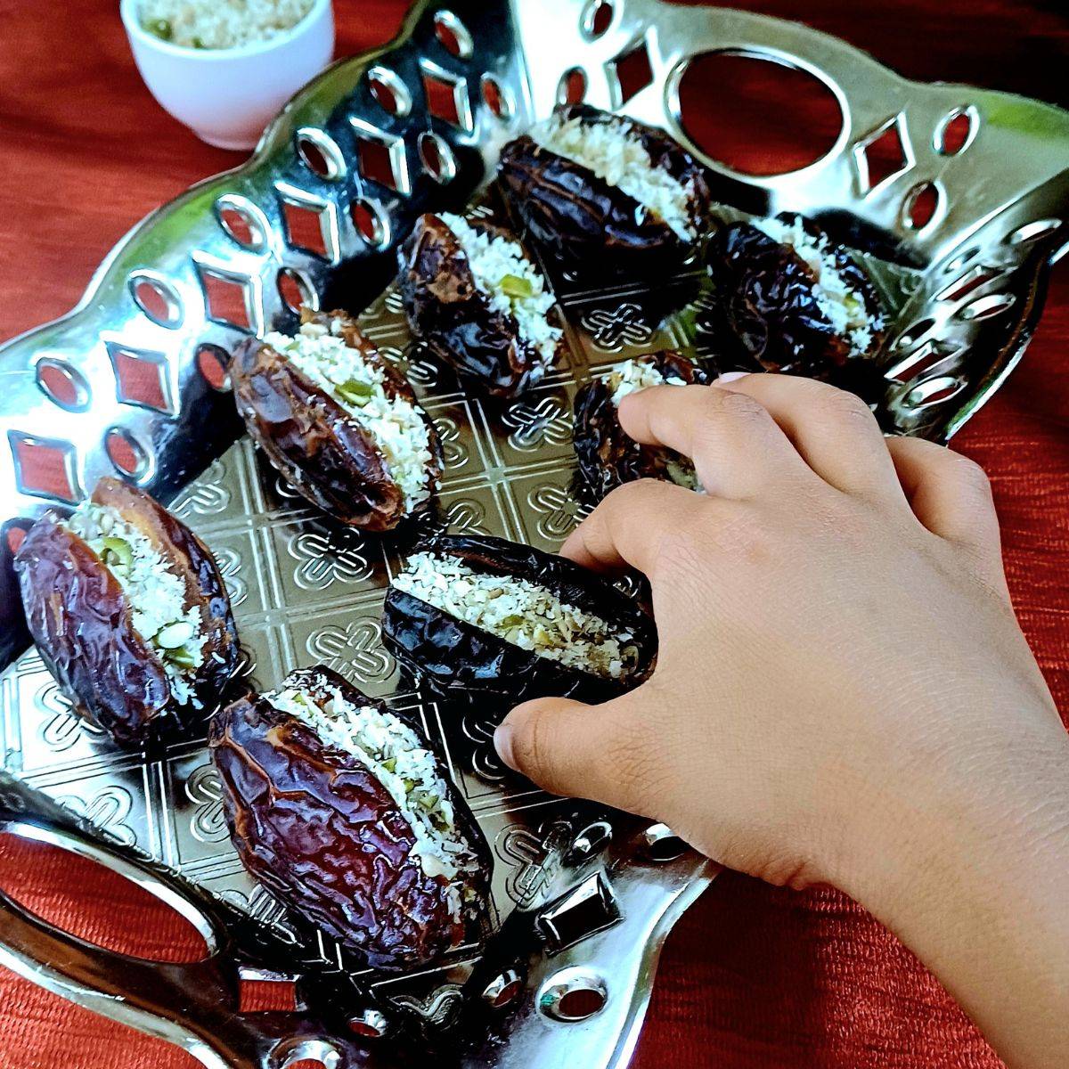 child picking up coconut superseed stuffed dates from a silver plate.