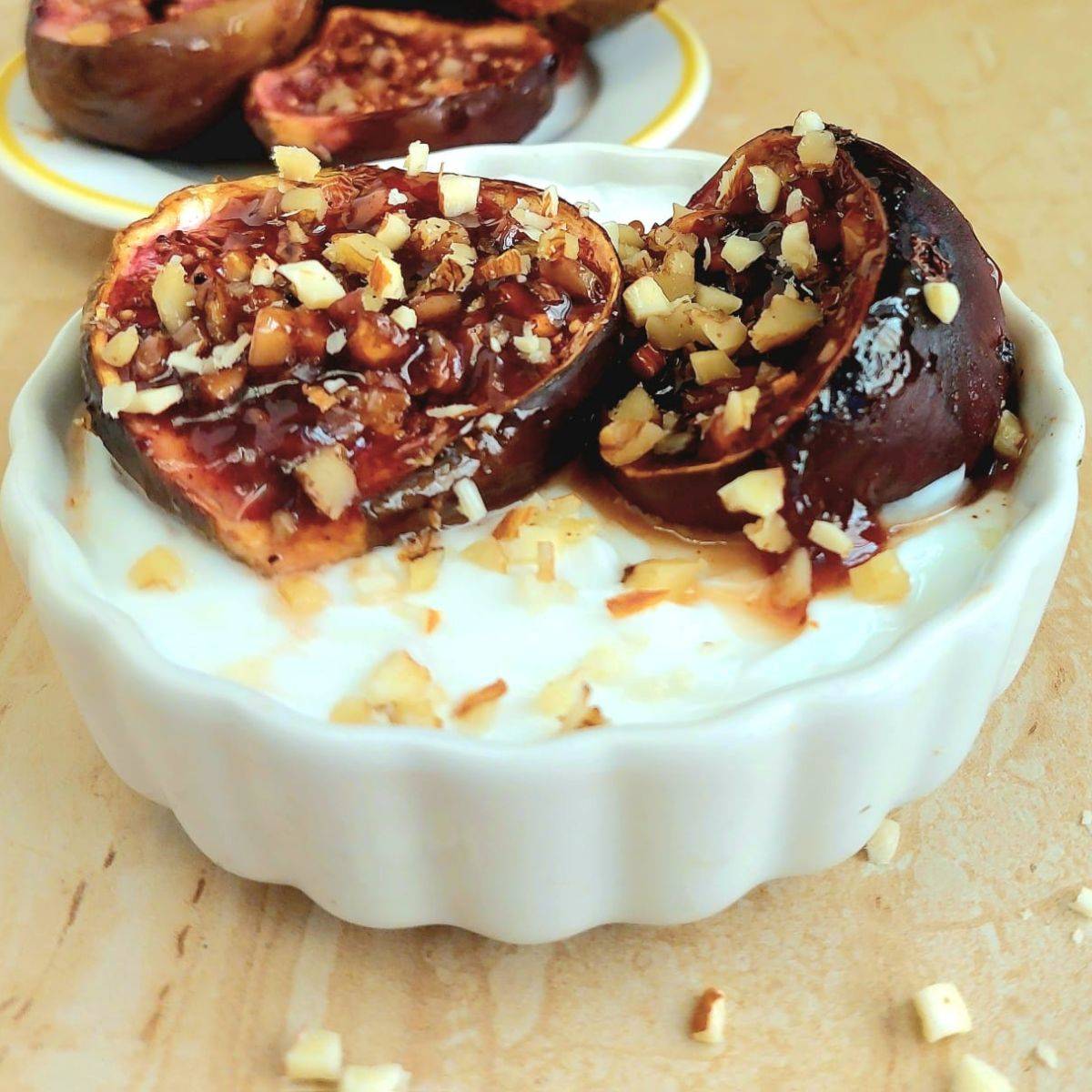white bowl of yogurt topped with roasted figs and nuts.