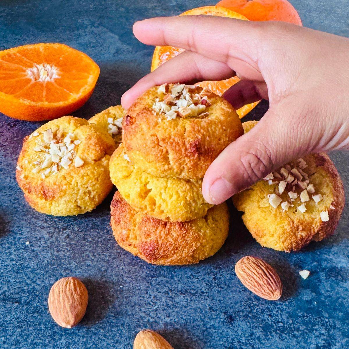 child picking orange almond cookies from the stack placed on granite along with cut oranges and almonds.