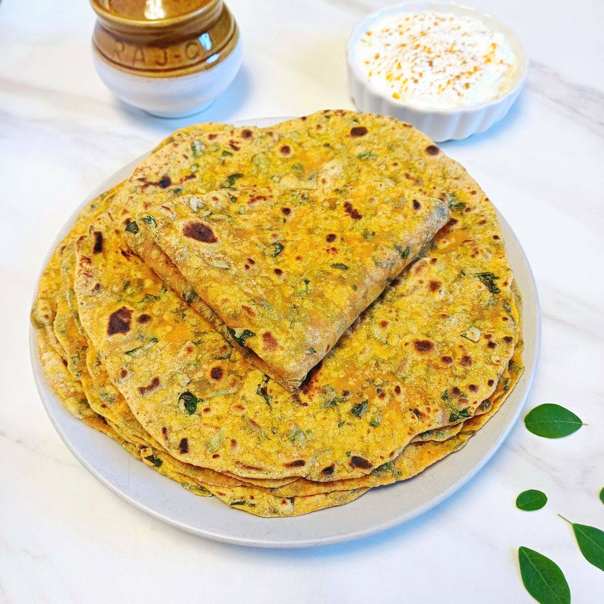 stack of moringa leaves paratha on grey plate placed on marble.