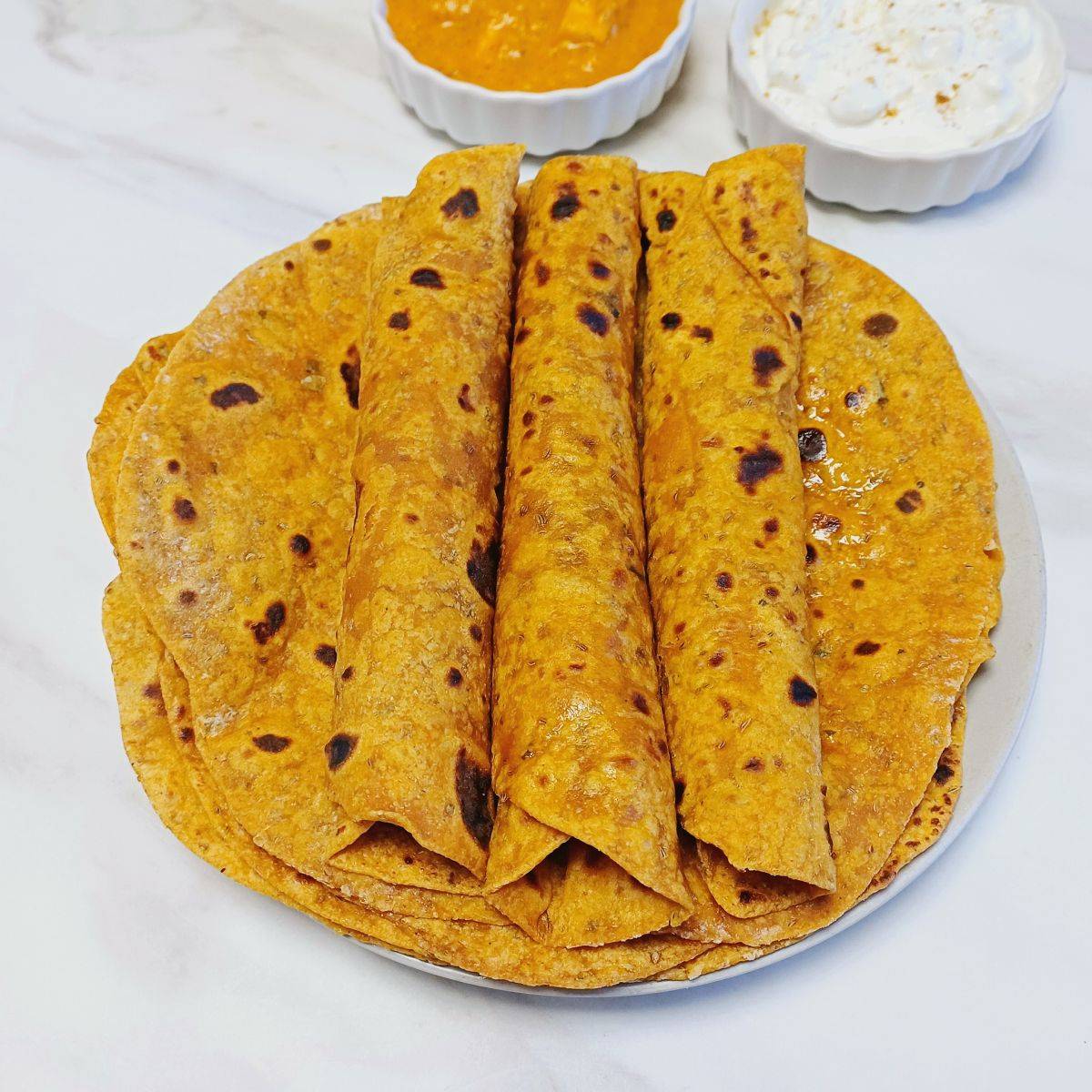 rolled up masala rotis on a grey plate placed on a marble.