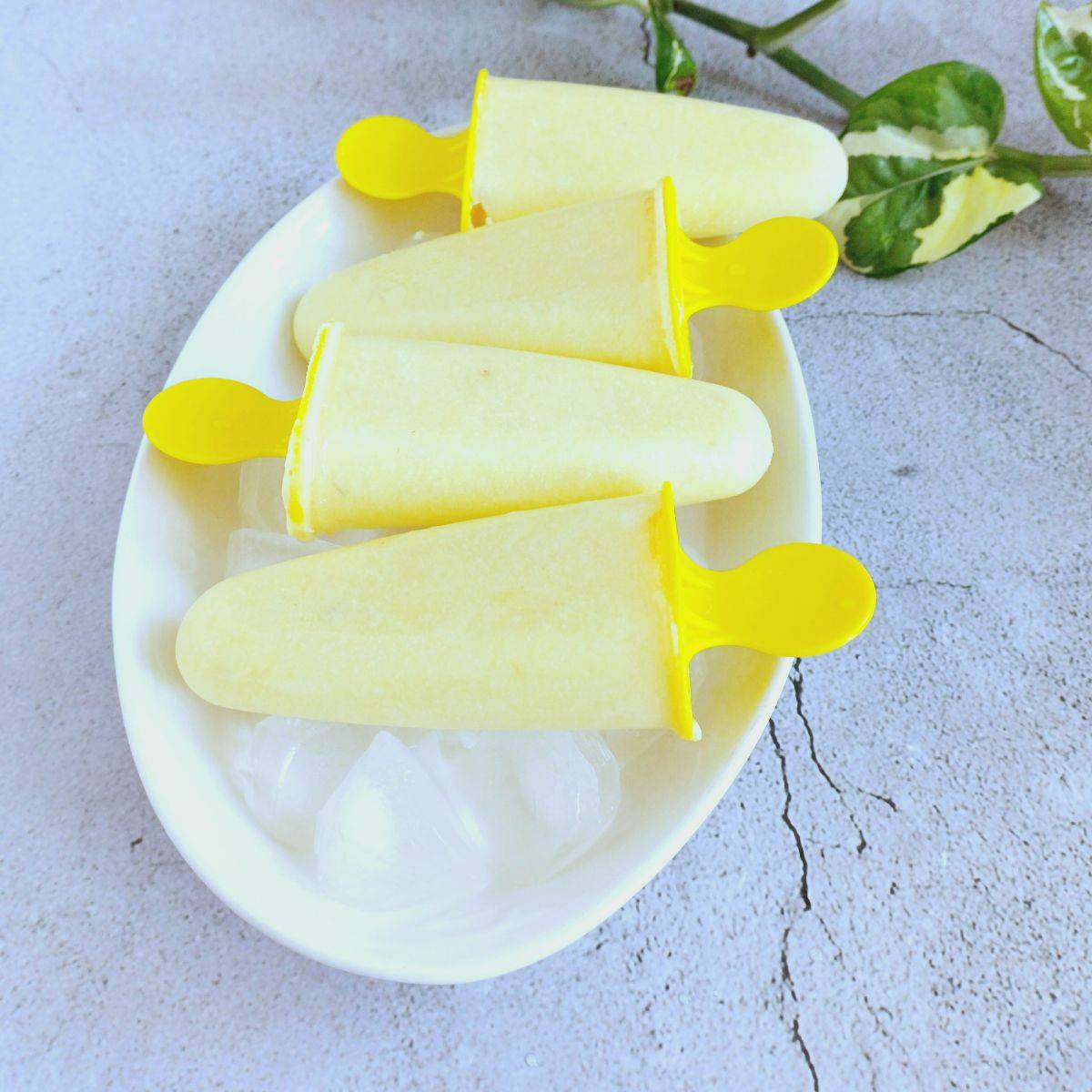 pineapple coconut popsicles placed on a white oval plate of bed of ice cubes. 