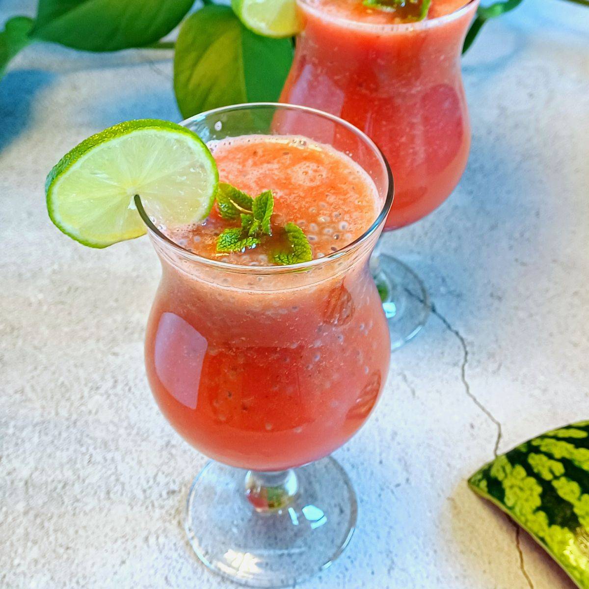 glass of watermelon cooler with basil seeds placed on blue backdrop along with a watermelon rind.