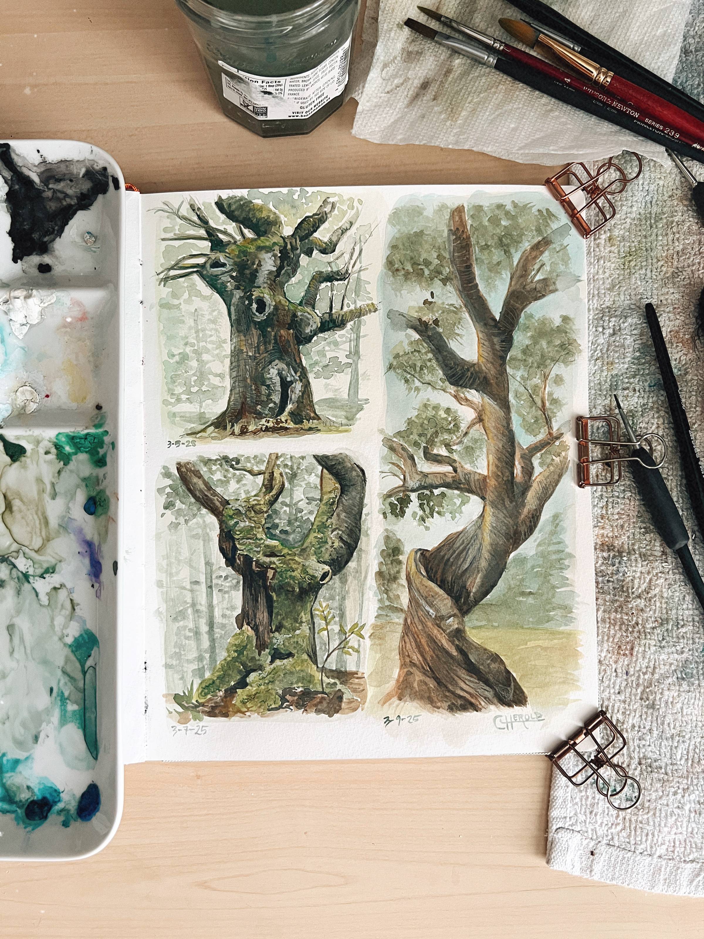 Three trees painted in gouache in a watercolor sketchbook. A palette of paint sits to the left of the notebook. Paintbrushes sit to the right.