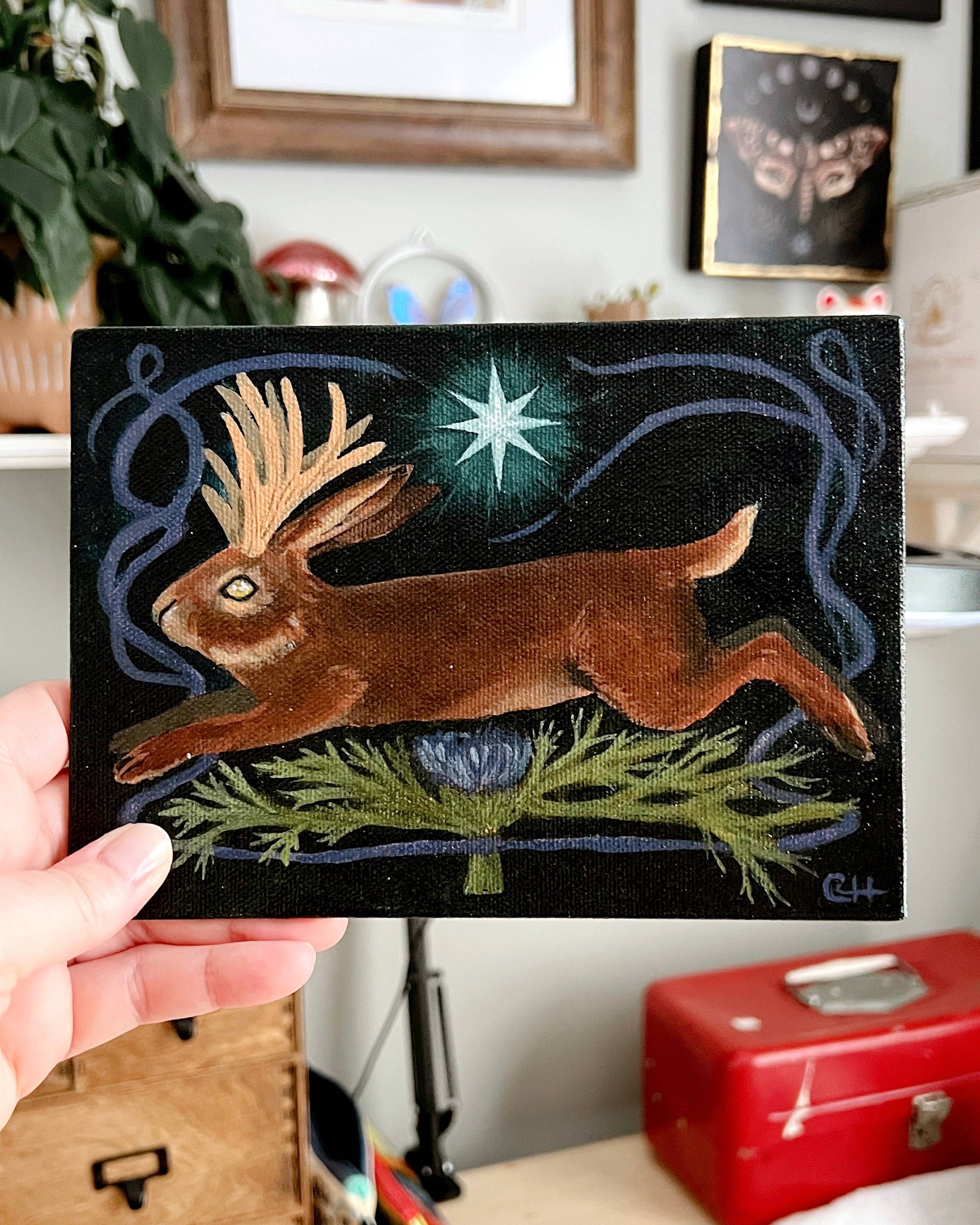 An oil painting of a brown jackalope and purple thistle. A glowing blue star is over the creature.