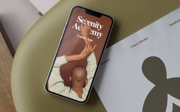 iPhone on green chair. iPhone screen says "Serenity Academy" Course App