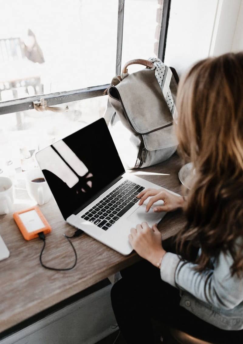 girl wearing grey long-sleeved shirt using MacBook Pro on brown wooden table