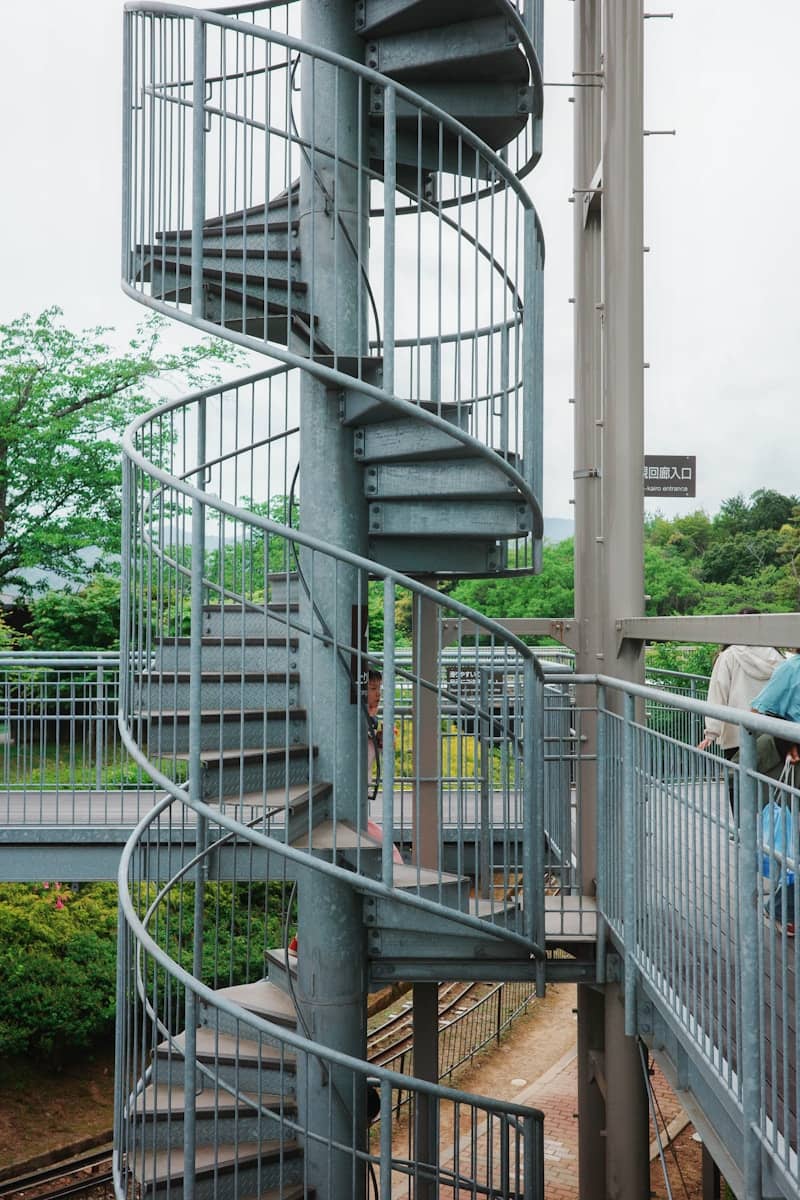 A metallic spiral staircase ascends outdoors.