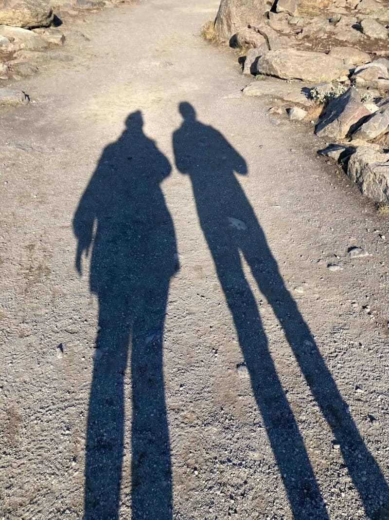 Two long shadows of people cast onto a rocky dirt path