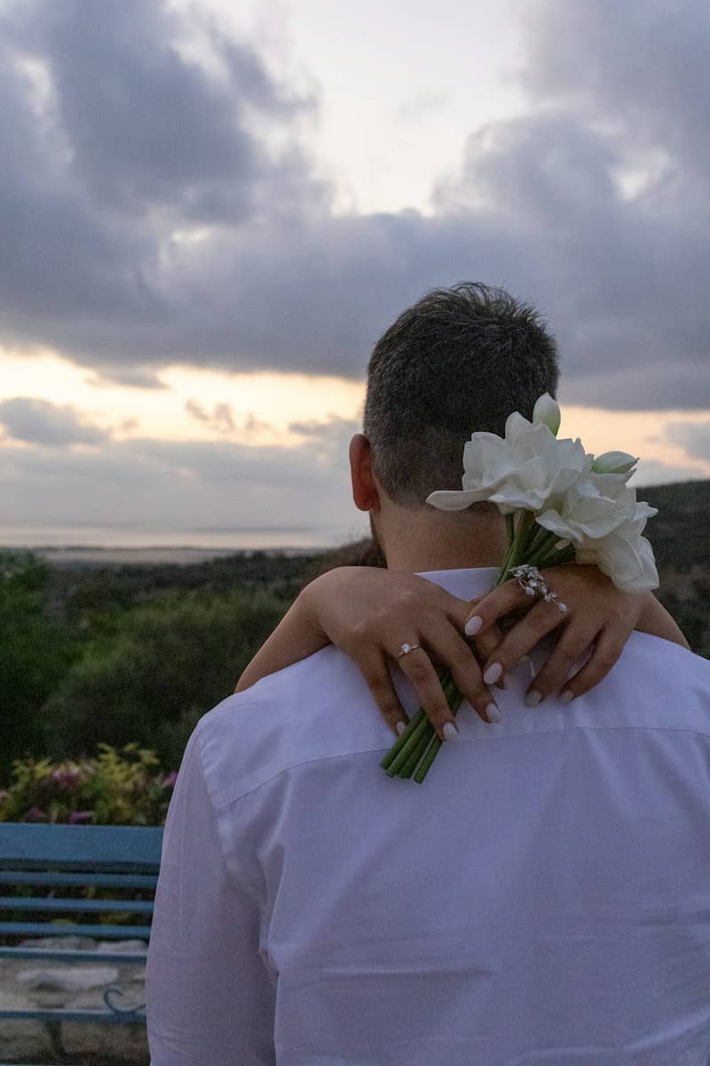 A person in a white shirt being embraced by arms holding white flowers