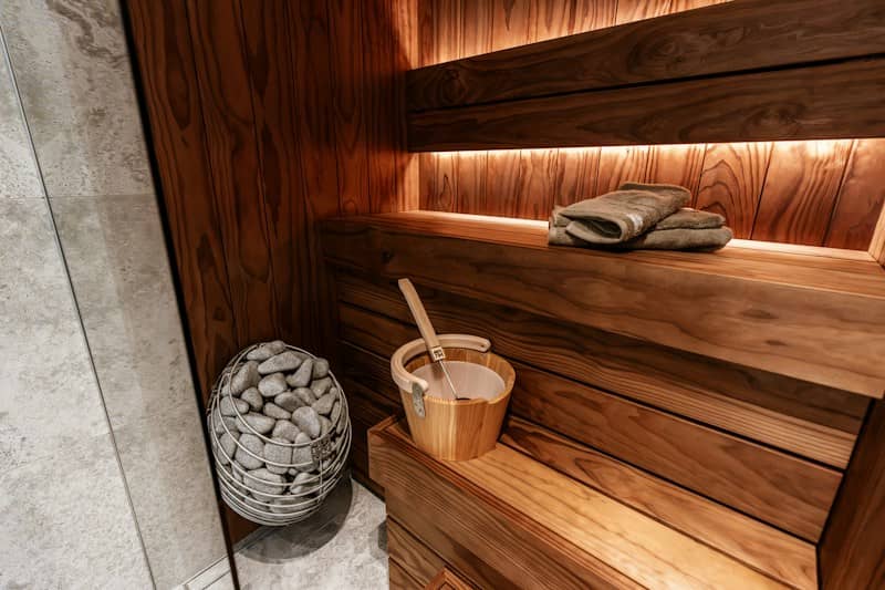 A wooden sauna interior with a bucket, ladle, and stones in a wire basket