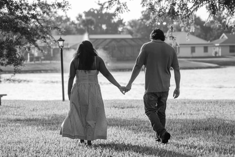 A couple holding hands walks towards a lake.