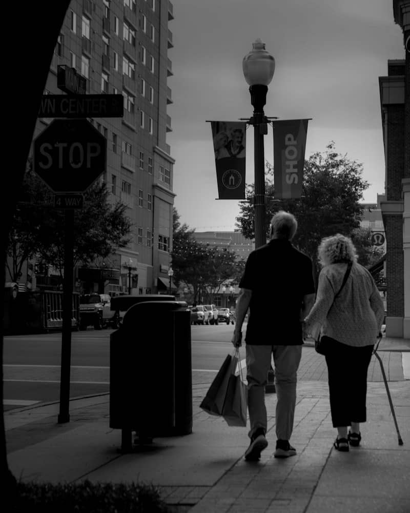Elderly couple walking on a city sidewalk with shopping bags.