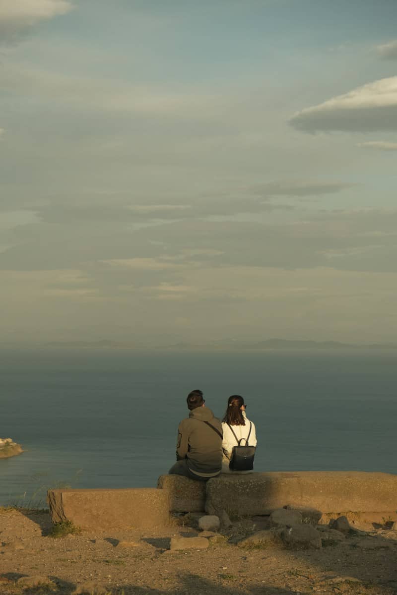 Two people on a stone wall overlooking the sea under a cloudy sky