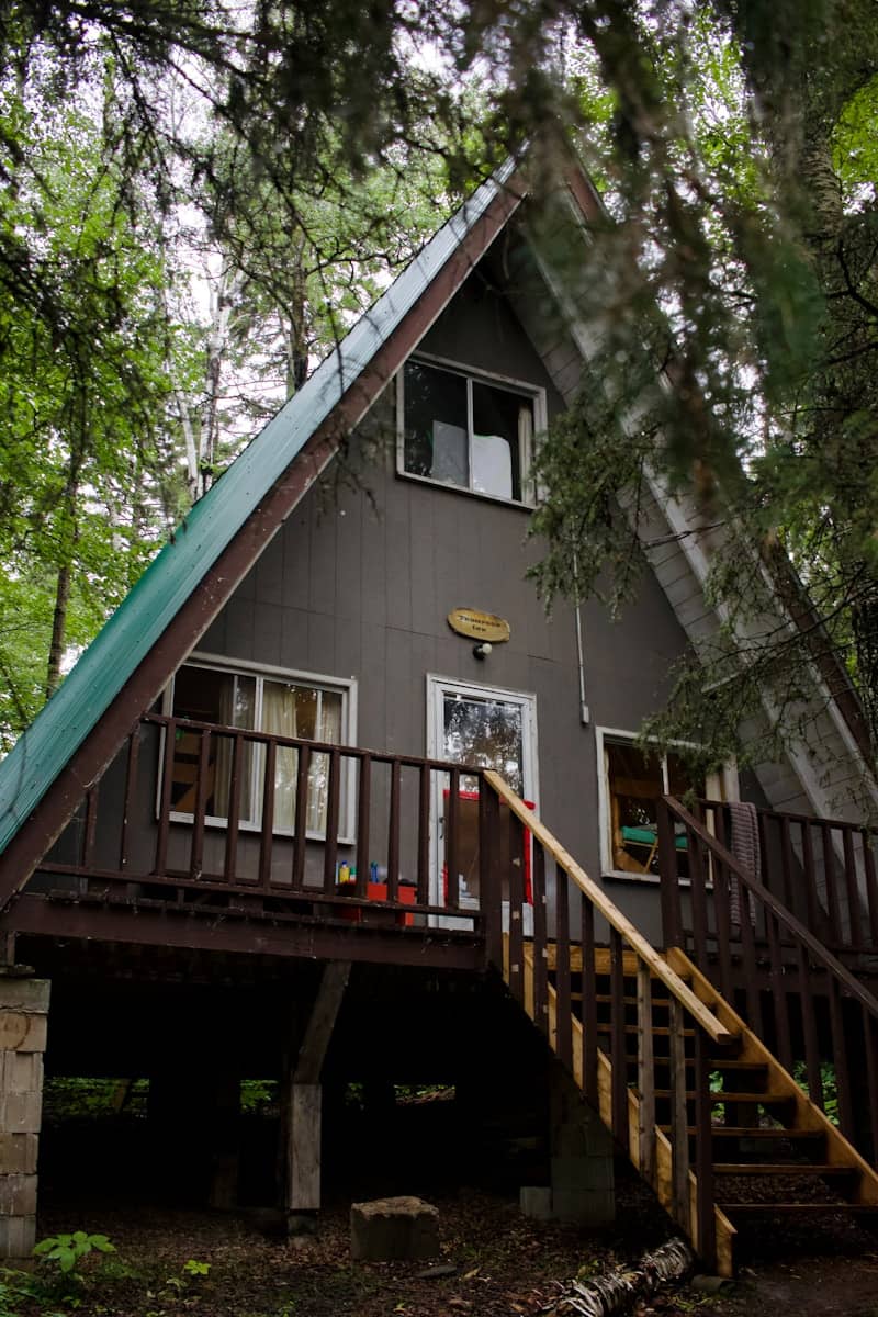 An a-frame cabin with a green roof in a forest.