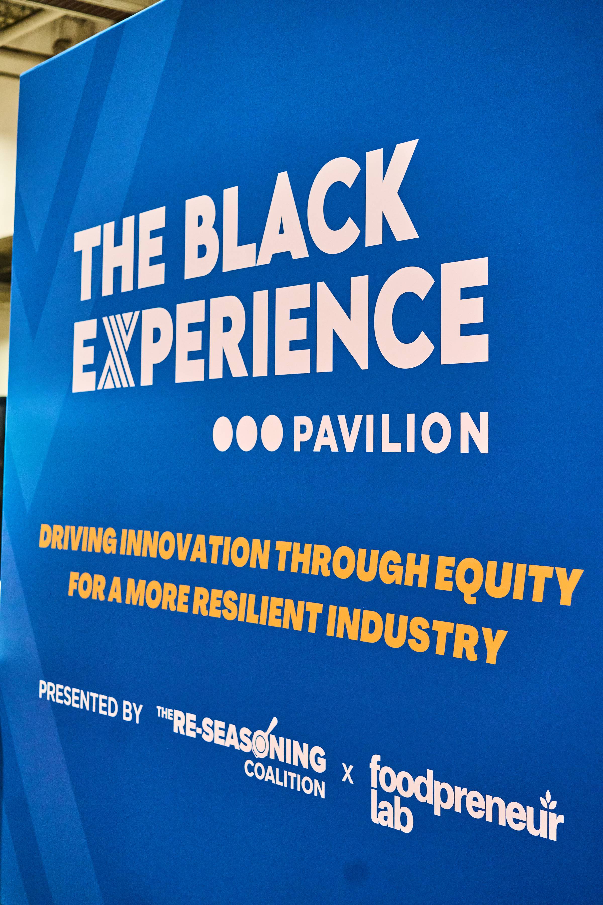a blue wall reading THE BLACK EXPERIENCE PAVILION, driving innovation through equity for a more resilient industry.