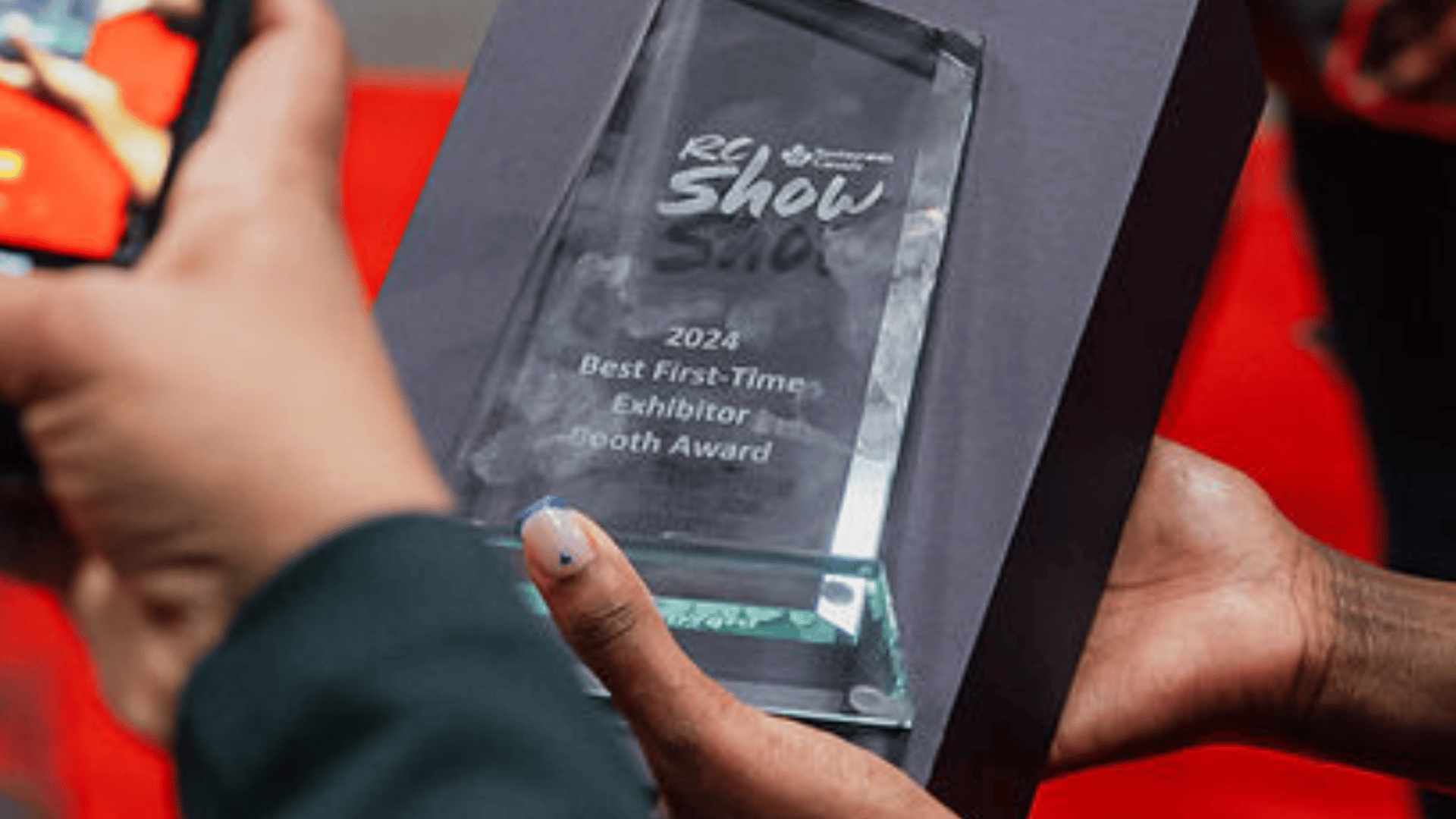 A glass award reading "RC Show 2024 Best First Time Exhibitor Booth Award"
